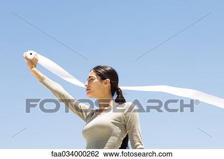 Woman holding up roll of paper outdoors, eyes closed, low angle view View Large Photo Image Stock Image - Woman holding up roll of paper outdoors, eyes closed, low angle view. Fotosearch