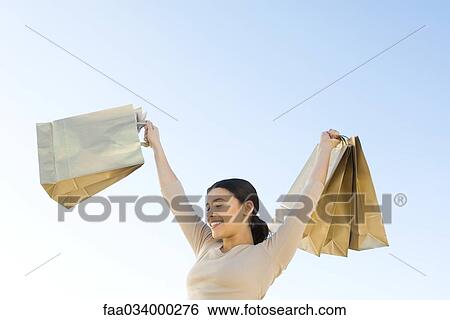 Stock Photograph - Woman holding up shopping bags, smiling, eyes closed. Fotosearch