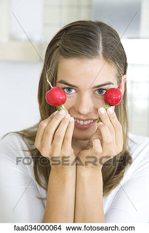 Picture - Woman holding up two radishes, smiling. Fotosearch