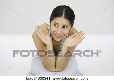 Stock Image - Woman leaning on elbows, hands open by face, smiling, looking away. Fotosearch