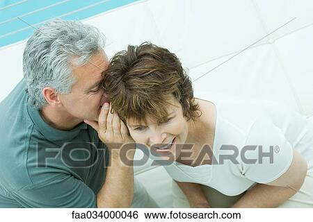 Stock Photograph - Woman looks away smiling as her husband whispers in her ear. Fotosearch