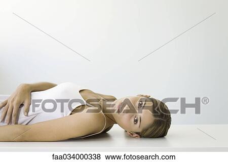 Stock Photo - Woman lying on back, hand on stomach, looking at camera. Fotosearch