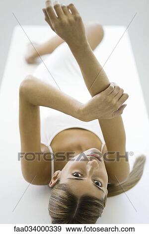 Stock Photo - Woman lying on back, one arm raised in the air, looking at camera. Fotosearch
