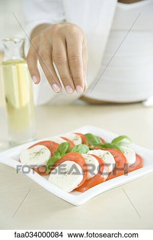 Woman preparing dish of Caprese salad, sprinkling pepper View Large Photo Image Picture - Woman preparing dish of Caprese salad, sprinkling pepper. Fotosearch