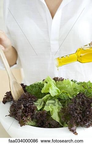 Stock Photograph - Woman preparing salad, pouring olive oil dressing . Fotosearch
