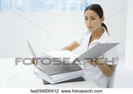Woman sitting at desk, looking at stacked binders View Large Photo Image Stock Image - Woman sitting at desk, looking at stacked binders. Fotosearch