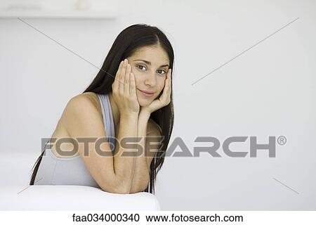 Stock Image - Woman sitting with chin in hands, smiling at camera. Fotosearch
