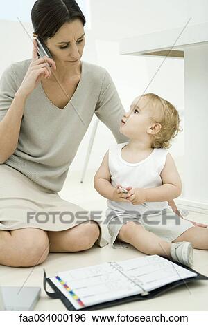 Stock Photograph - Woman sitting with toddler, using cell phone and looking down at agenda. Fotosearch