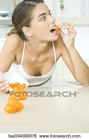 Stock Photograph - Woman spilling bowl of yellow cherry tomatoes, leaning on elbow, biting into one. Fotosearch