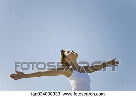 Stock Image - Woman standing outdoors with arms out, head back. Fotosearch