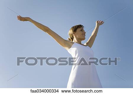 Woman standing outdoors with arms raised, smiling, low angle view View Large Photo Image Picture - Woman standing outdoors with arms raised, smiling, low angle view. Fotosearch