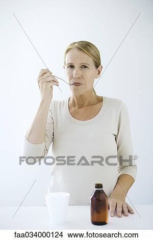 Woman taking spoonful of medicine, looking at camera View Large Photo Image Picture - Woman taking spoonful of medicine, looking at camera. Fotosearch