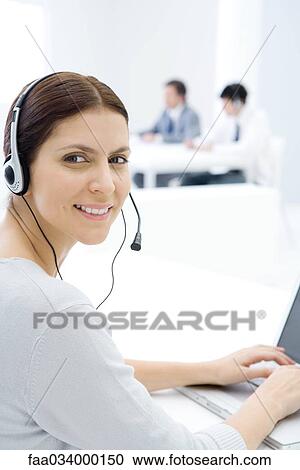 Woman wearing headset, working at desk, smiling over shoulder at camera View Large Photo Image Stock Image - Woman wearing headset, working at desk, smiling over shoulder at camera. Fotosearch