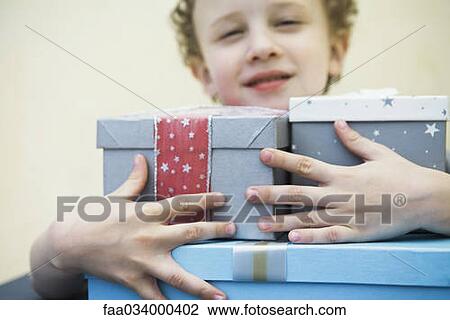 Stock Image - Young boy holding armful of gifts, smiling. Fotosearch