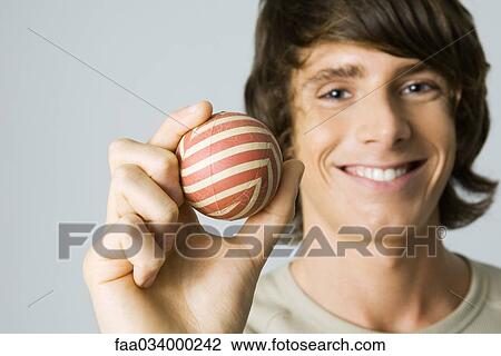 Stock Image - Young man holding striped ball, smiling at camera. Fotosearch