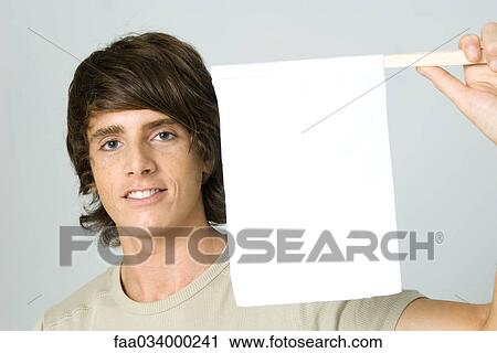 Stock Image - Young man holding up white flag, smiling at camera. Fotosearch