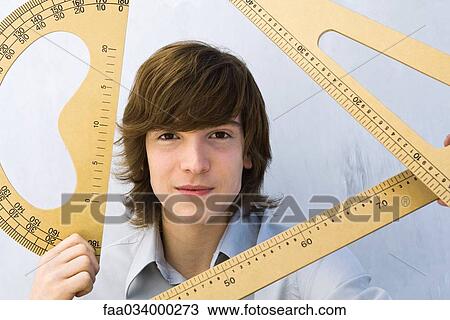 Stock Image - Young man holding various measuring instruments, smiling at camera. Fotosearch