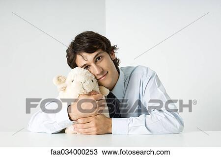 Stock Image - Young man hugging stuffed toy, smiling at camera. Fotosearch