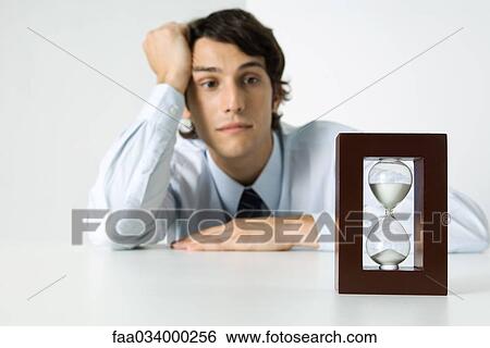 Young man looking at hourglass, holding head View Large Photo Image Stock Photograph - Young man looking at hourglass, holding head. Fotosearch