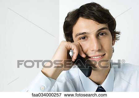 Stock Photo - Young man using cell phone, smiling at camera. Fotosearch