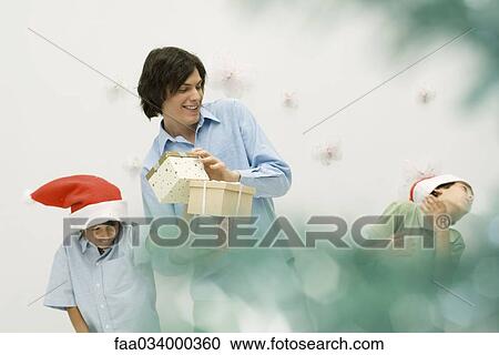 Stock Image - Young man with presents, playing with two boys wearing Santa hats. Fotosearch