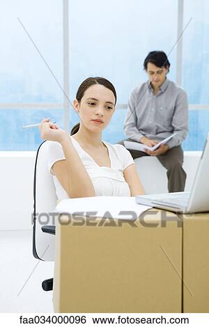 Young woman sitting at cardboard box desk, looking at laptop computer View Large Photo Image Stock Photograph - Young woman sitting at cardboard box desk, looking at laptop computer. Fotosearch