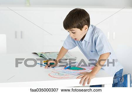 Stock Photo - Boy leaning on table, holding crayon, colorful drawing on paper and table. Fotosearch