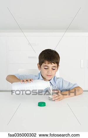 Stock Image - Boy pouring milk into empty glass. Fotosearch