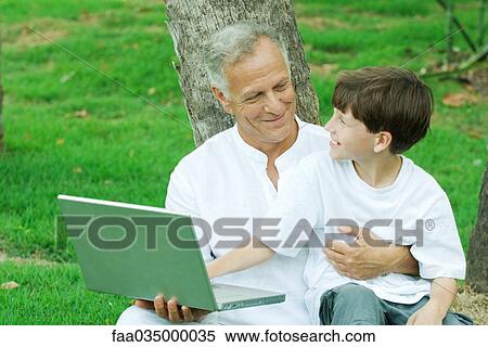 Boy sitting on grandfather's lap, using laptop computer View Large Photo Image Stock Photography - Boy sitting on grandfather's lap, using laptop computer. Fotosearch