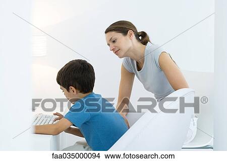 Boy typing on keyboard, mother looking over shoulder View Large Photo Image Picture - Boy typing on keyboard, mother looking over shoulder. Fotosearch