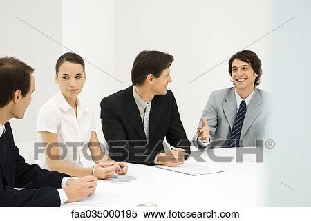 Business associates sitting around conference table, looking at each other, smiling View Large Photo Image Stock Photography - Business associates sitting around conference table, looking at each other, smiling. Fotosearch