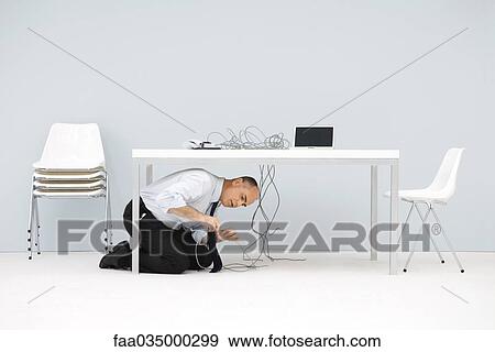 Businessman kneeling under table, examining cords View Large Photo Image Stock Photo - Businessman kneeling under table, examining cords. Fotosearch