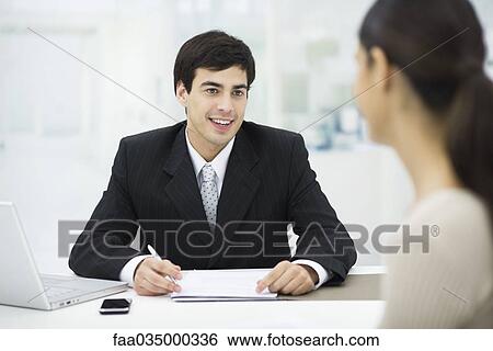 Stock Photograph - Businessman sitting at desk, talking with woman and smiling. Fotosearch