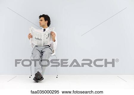 Businessman sitting in chair, holding newspaper, looking away View Large Photo Image Stock Photography - Businessman sitting in chair, holding newspaper, looking away. Fotosearch