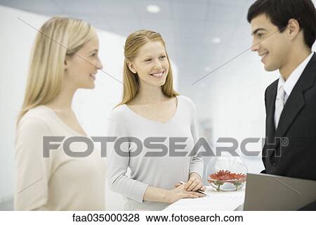 Businessman talking with two receptionists at counter, focus on women in center View Large Photo Image Stock Photo - Businessman talking with two receptionists at counter, focus on women in center. Fotosearch