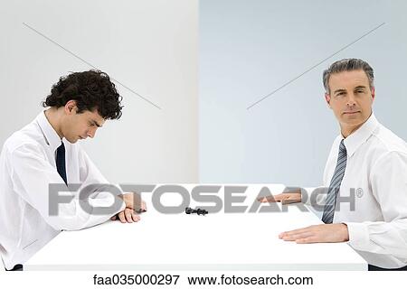 Businessmen sitting at table, tipped over chess piece between them View Large Photo Image Stock Photo - Businessmen sitting at table, tipped over chess piece between them. Fotosearch
