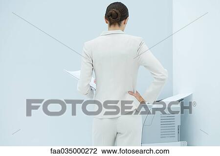 Businesswoman standing with hand on hip, looking at printer, rear view View Large Photo Image Stock Image - Businesswoman standing with hand on hip, looking at printer, rear view. Fotosearch