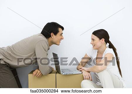 Couple sitting at makeshift desk with laptop computer between them, smiling at each other View Large Photo Image Picture - Couple sitting at makeshift desk with laptop computer between them, smiling at each other. Fotosearch