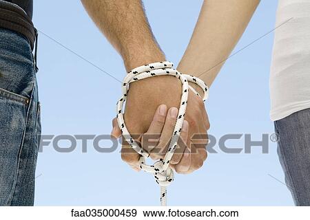 Stock Photo - Couple's hands bound together with rope, close-up. Fotosearch