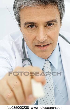 Stock Photo - Doctor holding tongue depressor toward camera, personal perspective. Fotosearch