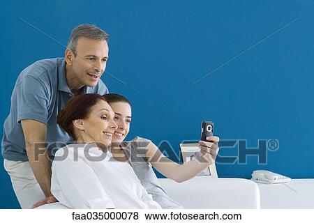 Stock Photo - Family leaning together for photograph, daughter hold out cell phone. Fotosearch