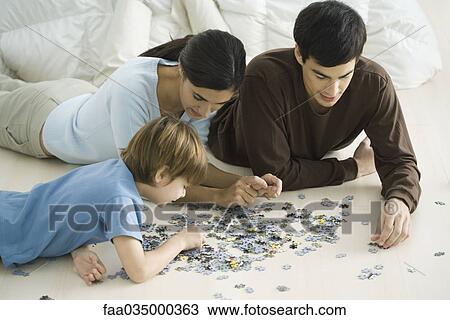 Stock Image - Family lying on floor, putting together jigsaw puzzle. Fotosearch