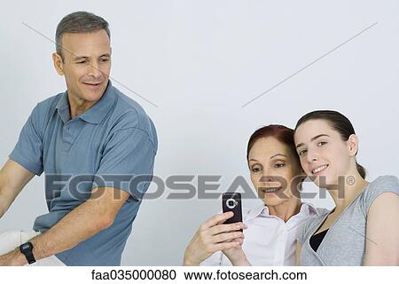Family sitting together, parents looking at cell phone, daughter smiling at camera View Large Photo Image Stock Image - Family sitting together, parents looking at cell phone, daughter smiling at camera. Fotosearch