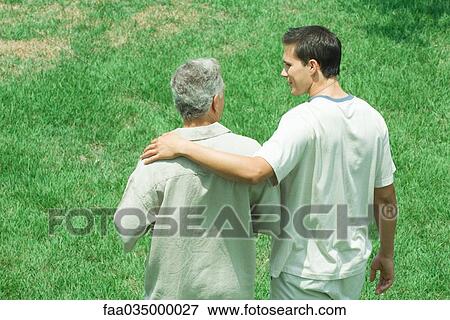 Stock Photo - Father and adult son walking together outdoors, rear view. Fotosearch