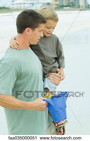 Father carrying son at the beach, plastic bucket in hand View Large Photo Image Stock Image - Father carrying son at the beach, plastic bucket in hand. Fotosearch