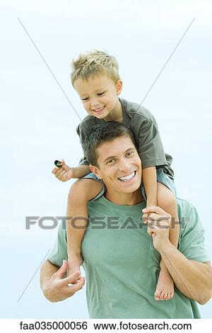 Stock Photograph - Father carrying son on shoulders, smiling at camera. Fotosearch