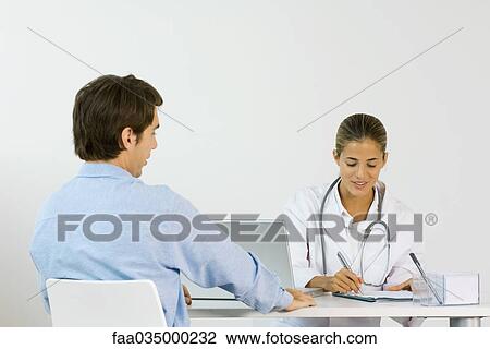 Female doctor sitting across from male patient at desk, writing down notes View Large Photo Image Stock Image - Female doctor sitting across from male patient at desk, writing down notes. Fotosearch