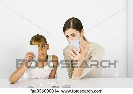 Girl and young woman sitting side by side, looking into hand mirrors, cosmetics in foreground View Large Photo Image Picture - Girl and young woman sitting side by side, looking into hand mirrors, cosmetics in foreground. Fotosearch