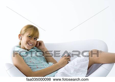 Stock Photo - Girl reclining in armchair, listening to MP3 player, smiling at camera. Fotosearch