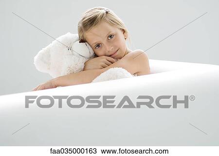 Stock Image - Girl sitting on sofa, hugging teddy bear, portrait. Fotosearch